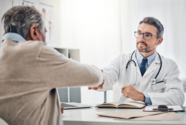 doctor shaking hands with his mature patient over the table